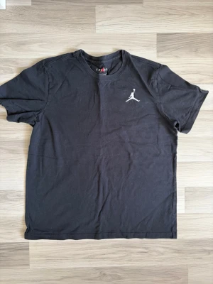 Svart Jordan t-shirt med logga - Snygg svart t-shirt från Jordan med den klassiska Jumpman-loggan broderad i vitt på bröstet. T-shirten har rund halsringning och korta ärmar. Perfekt för en sportig och avslappnad stil.