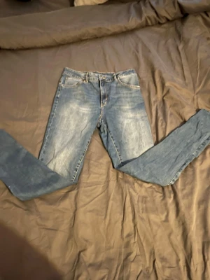 Blå slim fit jeans med slitningar - Säljer ett par blå slim fit jeans med lätt slitna detaljer och klassisk femficksdesign. Jeansen har normalhög midja och smala ben, perfekta till vardagslooken. Materialet är denim i bomull med lite stretch för skön passform.