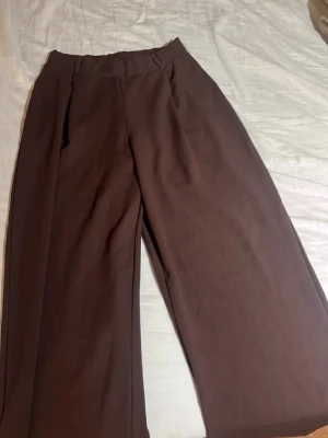 Bruna byxor  - Snygga bruna sköna byxor med hög midja och vida ben. Byxorna har pressveck framtill och bälteshällor i midjan. Perfekta för en stilren och trendig look. Materialet ser ut att vara mjukt och faller snyggt. Helt nya oanvända med prislapp kvar! Perfekta byxorna till hösten🍂🍁