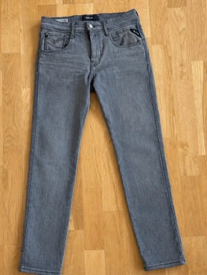 Grå slim jeans från Replay - Säljer ett par grå jeans från Replay med en slim passform och klassisk femficksdesign. Jeansen har bälteshällor och knappgylf. Materialet är mjukt denim som ger en avslappnad look. Perfekt för en grisch vardags outfit. 