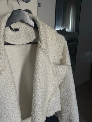Vit teddyjacka - Säljer en fluffig vit teddyjacka med och croppad passform. Jackan har en mjuk, lurvig yta och stängs framtill. Perfekt för dig som vill ha en mysig och trendig look till hösten eller vintern.