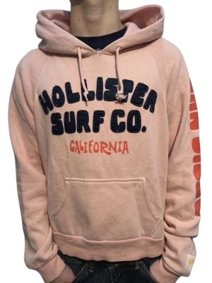 Hollister vintage hoodie rosa unisex - Säljer en fet rosa vintage hollister hoodie. Tröjan är unisex så passar perfekt till både tjejer och killar! Modellen är 163cm och väger 53kg, tröjan är i storlek S. Skicket är bra, inga fläckar eller hål. Några små defekter/små slitningar som är vintage stil men syns knappt! Unik fin hoodie!
