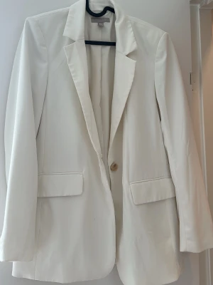 Vit oversized kavaj med fickor - Stilren vit kavaj i oversized modell med klassisk krage och två framfickor med lock. Kavajen har en knapp framtill och är helfodrad för extra komfort. Perfekt för en trendig och clean look.