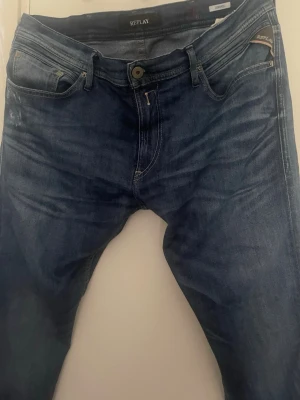 Mörkblå jeans från Replay - Snygga mörkblå jeans från Replay med klassisk femficksmodell och diskreta slitningar. Jeansen har raka ben och tydliga sömmar, perfekta för en avslappnad men stilren look. Materialet är mjukt denim som sitter skönt hela dagen.