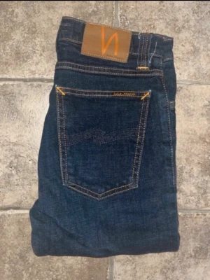 Nudie jeans  - Mörkblå skinny jeans från Nudie Jeans, modell High Kai. Hög midja och klassisk femficksdesign med orangea sömmar och läderpatch bak. Tillverkade i stretchig bomullsdenim för en tight passform. Midja 32cm, längd 99cm. Ifall det inte finns någon bild i annonsen där jag bär plaggen jag säljer så är det för att jag ej kan ha storleken heller passformen, så kolla måtten för storlek och googla på modellnamnet för passform 😉 OBS jeansen är uppklippta, se sista bilden. S4