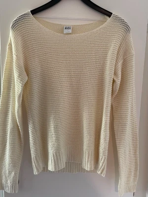 Cremevit stickad tröja från Vero Moda - Cremevit stickad tröja från Vero Moda. Tröjan har en luftig stickning och ribbade muddar vid ärmslut och nederkant. Längd: 60 cm. Axelbredd: 40 cm
