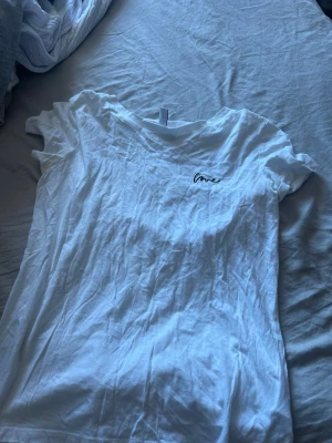 Vit t-shirt från Divided H&M XS - Vit t-shirt från Divided H&M i storlek XS. T-shirten har korta ärmar, rund halsringning och en liten svart broderad text 'love' på bröstet. Tillverkad i mjuk bomull, perfekt för en enkel och clean look.