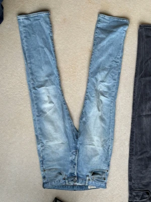 Levi's 501 ljusblå jeans - Klassiska Levi's 501 jeans i ljusblå denim med raka ben och knappgylf. Jeansen har en avslappnad passform och tydliga slitningar framtill för en cool vintagekänsla. Tillverkade i bomull och perfekta för en avslappnad streetstil.