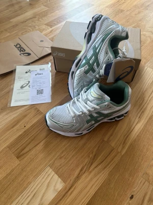 Asics gel kayano 14 - Snygga sneakers från Asics i vitt och grönt med mesh- och syntetmaterial. Skorna har klassisk Asics-logga på sidan, gröna detaljer och en chunky sula för extra komfort. Perfekta för dig som gillar sportig stil och vill ha något som sticker ut.
