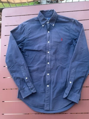Polo Ralph Lauren skjorta - Riktigt snygg Polo Ralph Lauren skjorta i storlek S. Ända defekten är att den är lite solblekt som ni kan se på bilderna. Annars fin marinblå färg med en röd polo logga. Riktigt skön o funkar perfekt nu inför sommaren. Pris går att diskutera vid snabb affär. Skickas inom 24h.