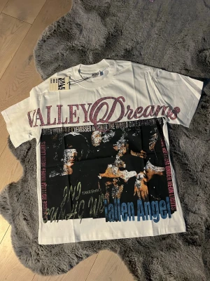 Valley Dreams Vit graphic T-shirt - Vit t-shirt med graphic design och tryck framtill där det står 'Valley Dreams' och 'Fallen Angel' i olika färger, samt rhinestones. T-shirten har korta ärmar och en avslappnad passform. Perfekt för dig som gillar streetwear och unika prints. Passar M bra och har generellt en perfekt boxig fit