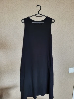 Svart ärmlös långklänning - En enkel och stilren svart långklänning med rund halsringning och ärmlös design. Klänningen har en rak passform och är tillverkad i ett mjukt material som ger en avslappnad look. Perfekt för dig som gillar minimalistisk stil.