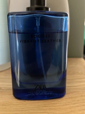 Zara Bogoss Vibrant Leather parfym - Zara Bogoss Vibrant Leather är en parfym i en stilren, djupblå glasflaska med svart spraymunstycke. Flaskan har en modern, rektangulär form och texten är tryckt i svart på framsidan. Perfekt för dig som gillar eleganta och fräscha dofter.