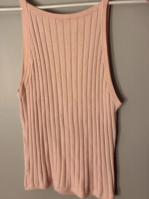 Ljusrosa ribbad linnetopp - Säljer en ljusrosa ribbad linnetopp med ärmlös design och rund hals. Perfekt för varma dagar och enkel att styla med olika outfits. Materialet känns mjukt och stretchigt.
