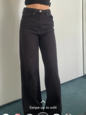 Svarta wide leg jeans - Säljer ett par svarta jeans med hög midja och wide leg-modell. Jeansen har klassisk femficksdesign och stängs med knapp och dragkedja. Perfekta för dig som gillar en avslappnad och trendig stil.