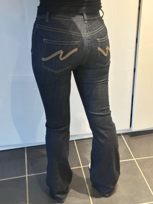 Mörkblå bootcut jeans med kontrastsömmar - Snygga mörkblå bootcut jeans med kontrastsömmar och dekorativa broderier på bakfickorna. Klassisk femficksmodell i denimtyg som sitter tajt över låren och släpper ut vid bensluten. Perfekta för en trendig och avslappnad look. Använt fåtal gånger så de är inte tvättade många gånger! (Är 168cm lång och jeansen går till hälen på mig)