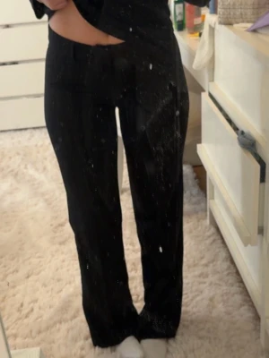 Svarta raka kostymbyxor - Säljer ett par svarta kostymbyxor med rak passform och klassisk midja. Byxorna har diskreta fickor och stängs med knapp och dragkedja. Perfekta för en clean och stilren look. Materialet ser ut att vara en mjuk och följsam mix, troligtvis polyester eller viskos.