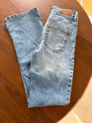 Ljusblå slitna jeans från ONLY - Säljer ett par ljusblå jeans från ONLY med klassisk femficksmodell och slitning på ena benet. Jeansen har något utsvängda ben, slits på insidan  och är tillverkade i mjukt denimtyg. Perfekta för en avslappnad och trendig look. Stl S/32. Djur finns i hemmet!