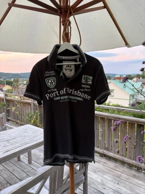 Pike från Camp David - Snygg pike från Camp David med vita och gröna tryck och broderade detaljer fram och bak. T-shirten har klassisk krage med vit kant, knappar vid halsen och korta ärmar med randiga muddar. Perfekt för en avslappnad och sportig stil.