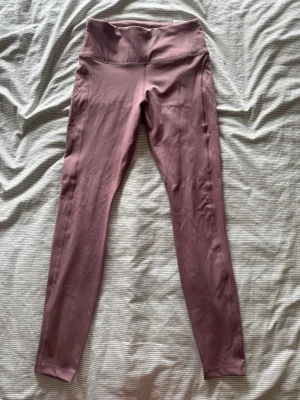 Rosa lilla Nike träningsbyxor - Träning tights från Nike. Dom har en ficka på ena sidan och en dragkedje ficka där bak. Dom är helt nya med lapparna på fortfarande. Nypris 650kr