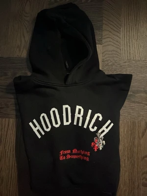 Svart hoodie från Hoodrich XL barn (13-15) - PRIS KAN DISKUTERAS🚨                                                                                 Svart hoodie från Hoodrich i storlek  (13-15Y) med stor vit logga på bröstet och texten 'From Nothing To Something' i rött. Hoodien har huva och en cool detalj med en liten röd och vit emblem. Perfekt för streetwear-stilen.