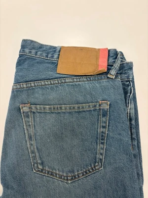 Acne jeans - Klassiska blå jeans i rak modell med hög midja och knappgylf. Jeansen har fem fickor och detaljer i kopparfärgade nitar. Tillverkade i slitstark denim, perfekta för en avslappnad och tidlös stil.