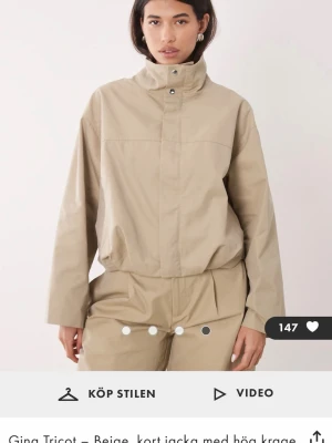 Beige vindjacka med hög krage - Stilren beige vindjacka med hög krage och dold dragkedja framtill. Jackan har en avslappnad passform, långa ärmar och elastisk nederkant. 