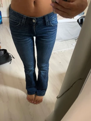Blå bootcut jeans från Gina Tricot - Snygga blå bootcut jeans från Gina Tricot i storlek 158. Jeansen har klassisk femficksmodell, normalhög midja och lätt utsvängda ben. Tillverkade i mjukt denimtyg med stretch för extra komfort. Perfekta för en trendig och avslappnad look. Byxorna saknar en av knapparna baktill men det är inget som märks så mycket
