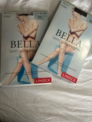 Bella semi glossy tights från Lindex - Två par Bella semi glossy tights från Lindex i färgen nearly black. Tightsen är 15 denier och har en lätt glansig finish. Tillverkade av 85% polyamid och 15% elastan för en bekväm passform.