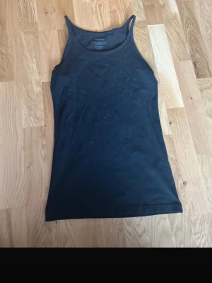 Svart linnetopp från Newbody - En enkel och stilren svart linnetopp från Newbody. Tillverkad i mjuk bomull med lite elastan för extra stretch. Klassisk passform med smala axelband och rundad halsringning. Perfekt basplagg till garderoben.