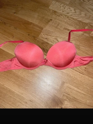 Rosa push-up bh med vaddering - Snygg rosa push-up bh med vadderade kupor och justerbara axelband. Bh:n har slät yta och stängs framtill med en liten rosett mellan kuporna. Perfekt för dig som vill ha extra lyft och stöd.