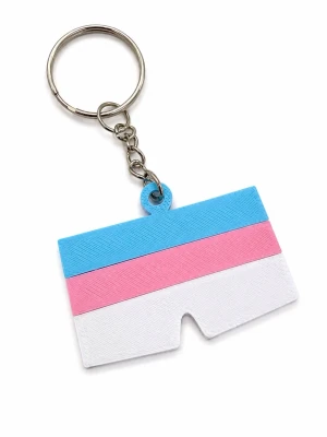 Nyckelring med transflagga - Säljer en unik nyckelring med motiv av transflaggan i blått, rosa och vitt. Nyckelringen har en rektangulär form med en liten urgröpning och är tillverkad i plast med metallkedja och ring. Perfekt att hänga på väskan eller nyckelknippan. Utmärkt till Pride eller annan tillställning 