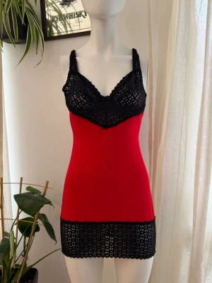 Vintage slip on klänning med lace - Snyggt nattlinne i rött med svarta virkade partier vid byst, axelband och nederkant. Figurnära modell med stretchigt tyg och dekorativa virkade detaljer som ger en unik look. Perfekt för dig som vill ha något både bekvämt och stilrent till natten.