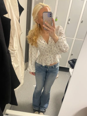 Vit blus med blått blommönster - Söt vit blus med små blå blommor, v-ringning och smockad midja som ger en fin siluett. Blusen har långa puffiga ärmar med resår vid handlederna och volang nedtill. Perfekt för en trendig och feminin look. Använd endast tre gånger!💓 pris går att förhandlas