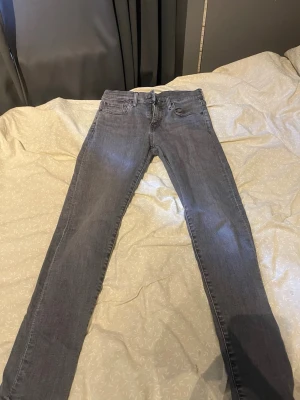 Grå slim fit jeans från Levi's - Snygga grå slim fit jeans från Levi's Premium med klassisk femficksdesign och dragkedjegylf. Jeansen har en modern passform och är tillverkade i mjukt denimtyg som sitter skönt hela dagen. Perfekta till en avslappnad streetstyle-look. Stl w28 L32