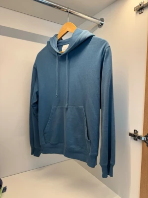 Stockholm Surboard Club hoodie - Säljer en riktigt snygg blå hoodie från Stockholm Surfboard Club i stl xs men passar också liten s. Köpt i butik för 3000kr och varsamt använd. Tröjan är i topp skick förutom ett litet hål vid fickan som inte syns vid användning.