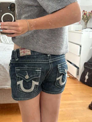 True Religion shorts  - Säljer ett par mörkblå True Religion shorts för att de är för stora för mig. Shortsen har låg midja, knappgylf och dekorativa knappar på fickorna. Perfekta för sommaren och ger en avslappnad men trendig look.