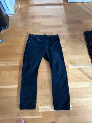 Svarta raka jeans - Snygga svarta Levis 501 jeans med rak passform . Jeansen har svarta sömmar och knappgylf. Passar perfekt till en avslappnad streetwear-look och är lätta att matcha med olika stilar. Storlek 33/30