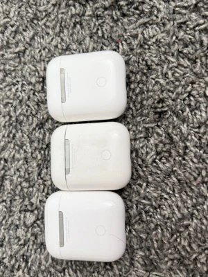 Trådlösa vita hörlurar med laddningsetui - Säljer tre par trådlösa vita hörlurar med tillhörande laddningsetui. Hörlurarna har en stilren och kompakt design med rundade kanter och magnetiskt lock. Perfekta för musik, poddar och samtal på språng. Materialet är blank plast och de är enkla att ta med sig överallt.
