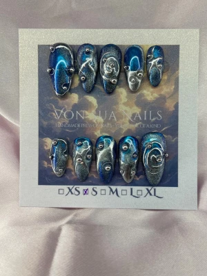 Zenith (S);Medium Almond - Unika press-on naglar i storlek S: 15 mm, 11,5 mm, 12 mm, 11 mm, 9 mm , med blå cateye/metallic bas och handmålad silver swirl-design. Naglarna har 3D-detaljer i form av små silverpärlor och abstrakta mönster. Formen är medium lång almond och finishen är glansig. Perfekt för dig som vill sticka ut med en kreativ och konstnärlig look.S: 15 mm, 11,5 mm, 12 mm, 11 mm, 9 mm 