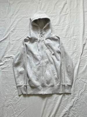 Ljusgrå zip hoodie med huva från russemerch - Ljusgrå hoodie med dragkedja framtill och stor känguruficka. Tröjan har en klassisk huva med dragsko och ribbade muddar vid ärmar och nederkant. Tillverkad i mjukt sweatshirtmaterial som är perfekt för chill dagar.