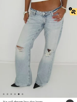 Ljusblå slitna low rise jeans - Säljer ett par ljusblå low rise jeans med raka ben och slitningar på båda knäna. Jeansen har en avslappnad passform och är tillverkade i klassiskt denimtyg. Perfekta för en trendig och avslappnad look.