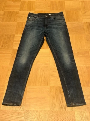 Mörkblå slim fit jeans - Snygga mörkblå slim fit jeans med sköna fades på framsidan och klassiska fem fickor. Jeansen har en rak passform och kontrastsömmar. Perfekta till en avslappnad stil och passar till det mesta i garderoben. Storlek: 33 x 32