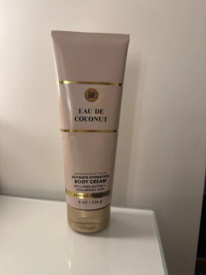 Eau De Coconut Body Cream - Lyxig body cream med doft av kokos, sheasmör och hyaluronsyra för intensiv återfuktning i upp till 48 timmar. Tuben är beige med gulddetaljer och rymmer 226 g. Perfekt för dig som vill ha mjuk och återfuktad hud med en fräsch kokosdoft. Använd 2 gånger typ 