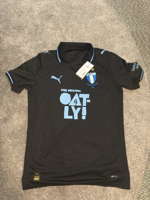Svart Malmö FF matchtröja Puma - Snygg svart matchtröja från Malmö FF med ljusblå detaljer och klubbmärke på bröstet. Tillverkad i funktionsmaterial med Oatly-logga på magen och Puma-logga på axel och bröst. Perfekt för fotbollsträning eller att bära på läktaren.