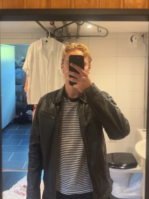 Svart klassisk skinnjacka - Säljer en svart skinnjacka med klassisk rak passform och dragkedja framtill. Jackan har två bröstfickor med dragkedja och en enkel krage. Suverän nu t hösten
