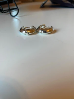 Silvriga chunky hoops örhängen - Säljer ett par silvriga chunky hoops örhängen i rund, klassisk form. De är blanka och har en enkel, stilren design som passar till många olika looks. Perfekta för dig som gillar minimalistiska smycken med lite extra edge. Aldrig använda. 