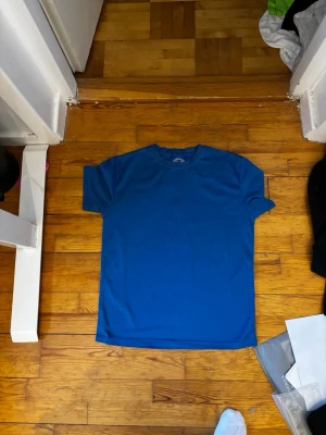 Blå t-shirt från Ravelli - En enkel och stilren blå t-shirt från Ravelli i 100% polyester. T-shirten har rund halsringning och korta ärmar, perfekt för en clean och sportig look. Passar dig som gillar basic plagg med skön passform.