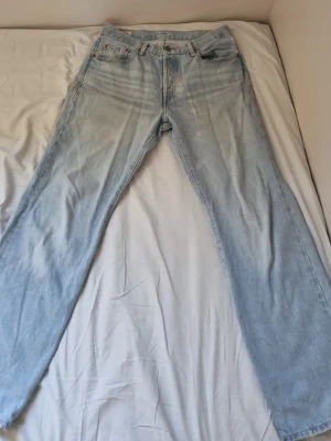 Ljusblå Levi's 501 jeans - Säljer ett par klassiska ljusblå Levi's 501 jeans med rak passform och fem fickor. Jeansen har den ikoniska läderlappen bak i midjan och röd Levi's-tag på bakfickan. Tillverkade i slitstark bomullsdenim och perfekta för en avslappnad look.