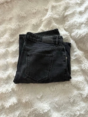 Svarta raka jeans med hög midja - Säljer ett par svarta jeans med raka ben och hög midja. Jeansen har klassisk femficksdesign och är tillverkade i ett robust denimtyg. Perfekta för dig som gillar en avslappnad och trendig stil.
